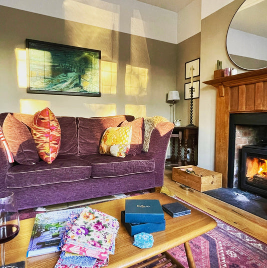 Image showing modern items mixed with vintage in a living room; Ercol coffee table, vintage artwork, candlesticks and side tables sit beside a new sofa, rug and mirror. 
